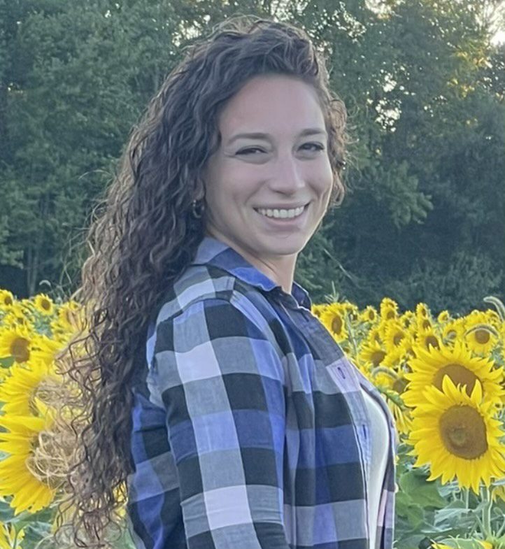 A woman standing in front of sunflowers smiling.